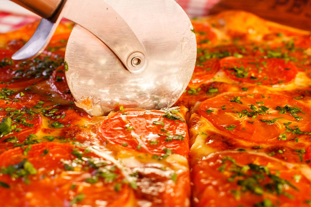 Close up Cuts with a pizza cutter. Pizza Margarita. Delicious hot food sliced and served on white platter. Menu photo, Italian fast food. - Photo, Image