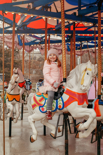 Adorable niña caucásica sonriente montar en alegre ir caballo carrusel en Navidad mercado de invierno al aire libre. Niño feliz divirtiéndose celebrando el Año Nuevo
.  - Foto, imagen