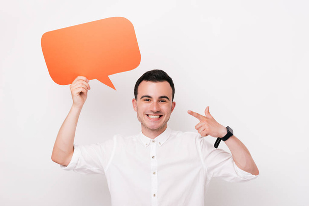 Cheerful young man holding a dialog cloud or rectangular  orange bubble speech on white background. - Photo, Image