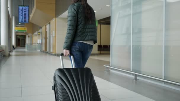 Cestujícímu žena kráčí v moderním letištním terminálu s kufříkem, pohled zpět. - Záběry, video