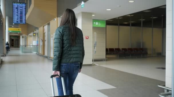 Cestujícímu žena kráčí v moderním letištním terminálu s kufříkem, pohled zpět. - Záběry, video