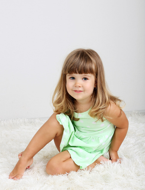 Little cute girl sitting on carpet, on gray background - Foto, immagini