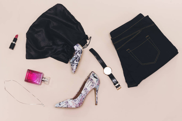 czarny Jean, srebrny zegarek, różowe butelki perfum, różowy szminka, buty pompy w czarnej torbie - Zdjęcie, obraz