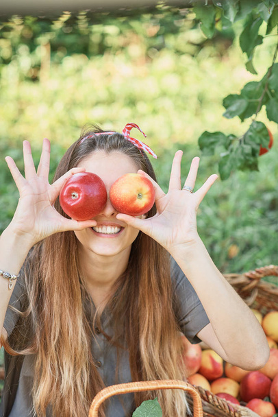 Girl holding apples in front of eyes while standing in orchard. Harvest concept - Foto, Imagen