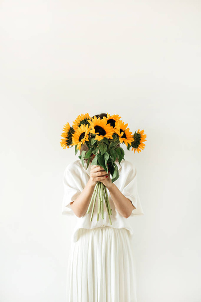Jovem mulher bonita em vestido branco segurar girassóis buquê no fundo branco. Florista conceito mínimo
. - Foto, Imagem