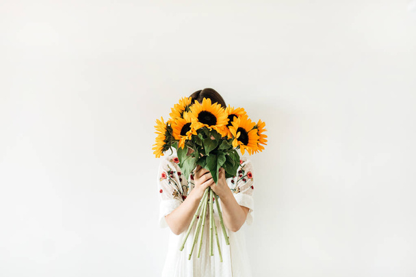 Giovane bella donna in abito bianco tenere bouquet di girasoli su sfondo bianco. Composizione floreale minima
. - Foto, immagini