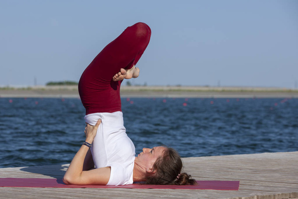 Young girl practices yoga on the shore of the lake, the concept of enjoying privacy and concentration, sunlight - Foto, Bild