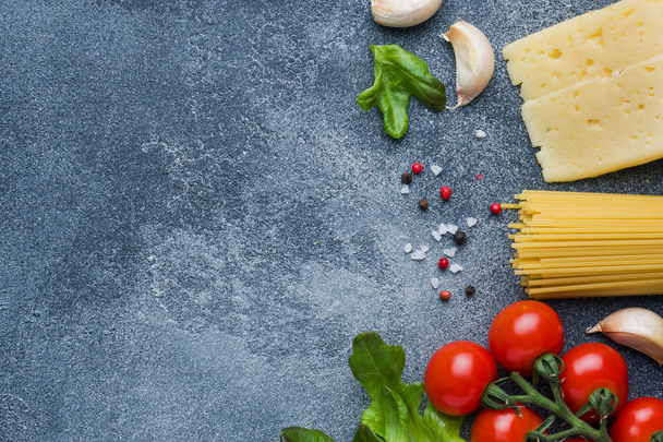 Raw Italian pasta spaghetti and cooking ingredients cherry tomatoes Cheese greens. Italian food dark stone background. Top view with copy space - Foto, imagen