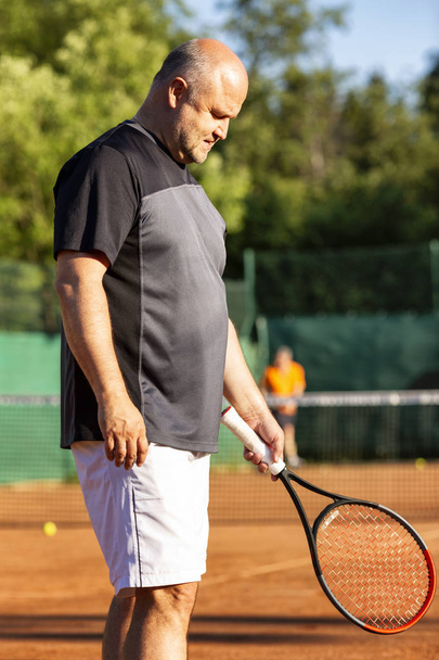 A middle-aged bald man plays tennis on the outdoor court. Sunny day.  - Photo, Image