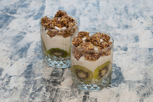 Granola, kiwi, banana e iogurte grego em copos de vidro em concreto cinza
 - Foto, Imagem