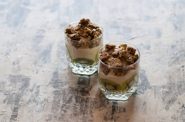 Granola, kiivi, banaani ja kreikkalainen jogurtti lasikupeissa harmaalla betonilla
 - Valokuva, kuva