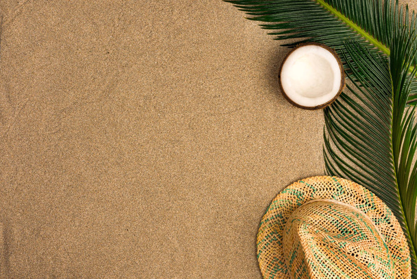  Beach theme on the sand background. Palm leaves, coconut, hat on the sand. Top view. - Foto, Imagem