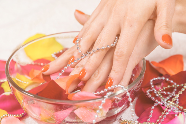 mains mouillées dans un bol avec des ongles rouges sur les pétales de rose
 - Photo, image