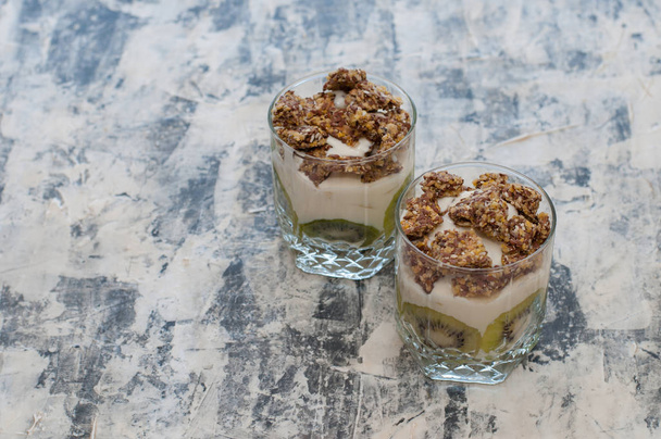 Granola, kiwi, banana and greek yogurt in glass cups on gray concrete - Fotografie, Obrázek