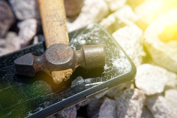 Vetro rotto di smartphone con martello su pietre di ghiaia. Focus selettivo e luci del fascio solare
 - Foto, immagini