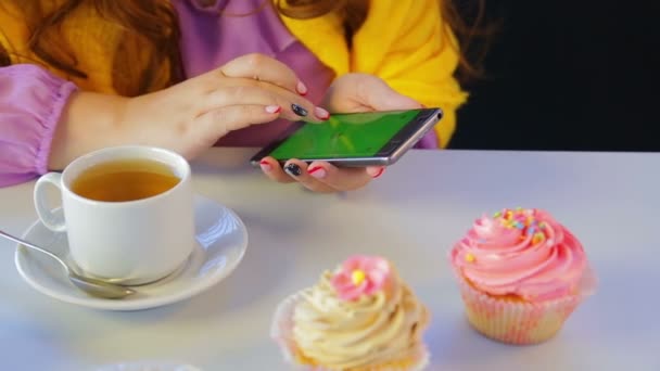 The girl in a cafe at the table with cakes leafing through the news in the smartphone. - Filmati, video