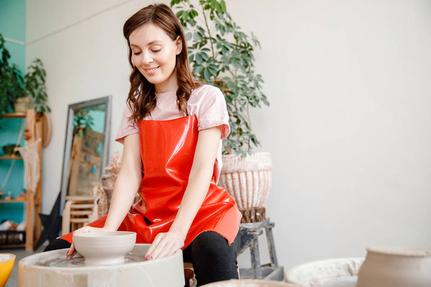 Work potter wheel. Happy young woman in red apron sculpts from clay - Foto, Imagen