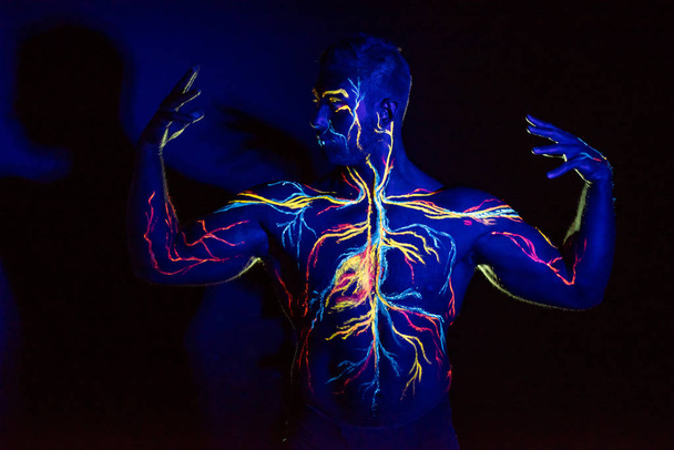 UV patterns body art of the circulatory system on a man's body. On the chest of a muscular athlete, veins and arteries are drawn with fluorescent dyes. The bodybuilder straightened the biceps - Foto, Imagem