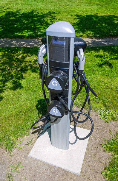 Точка зарядки электромобиля установлена на зеленой лужайке в солнечный день
 - Фото, изображение
