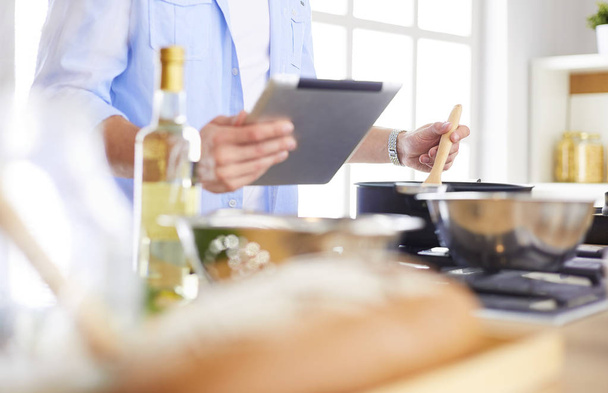 Man following recipe on digital tablet and cooking tasty and healthy food in kitchen at home - Photo, image