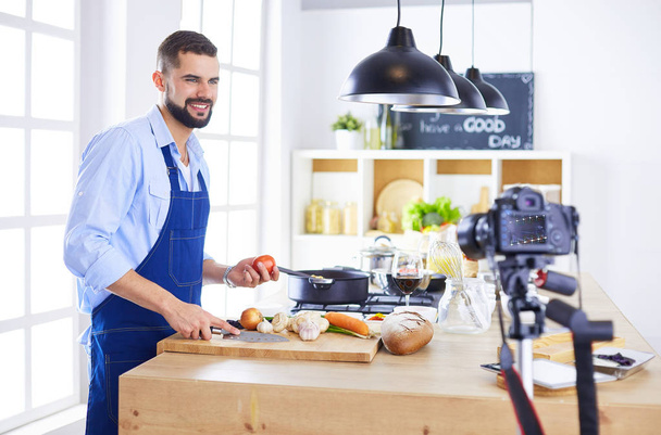 Hombre sosteniendo bolsa de papel llena de comestibles en el fondo de la cocina. Compras y concepto de comida saludable - Foto, Imagen