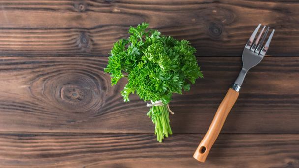 Bunch of parsley tied with a rope and a fork on a wooden table. Flat lay. - Foto, Imagem