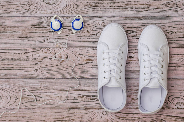 Zapatillas blancas y auriculares azules en el suelo de madera. Estilo deportivo. Puesta plana
. - Foto, imagen