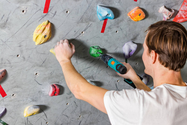 Rock climber fastens the hook with a screwdriver at the climbing wall in the boulder hall - Foto, Imagen