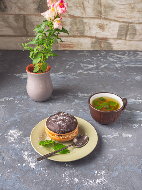 Cake bouche on a small plate with a mug of tea and a mashine flower snapdragon in a clay cup - Fotoğraf, Görsel