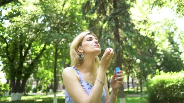 Mujer bonita soplando burbujas de jabón en el parque de la ciudad de verano, cámara lenta. Disparo constante
 - Metraje, vídeo