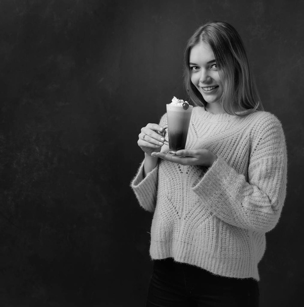 Hermosa rubia en un suéter sosteniendo una taza de café con crema
 - Foto, imagen