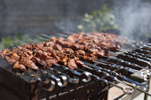 La viande sur les brochettes est rôtie sur le feu. Cubes de viande grillés sur brochette en métal. Viande avec fumée sur un barbecue au charbon de bois
. - Photo, image