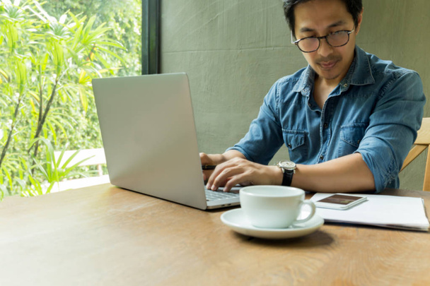 Mann mit Brille arbeitet am Laptop mit Kaffeetasse auf Holztisch. - Foto, Bild