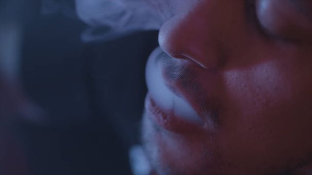Close-up voor de man het roken van een waterpijp, uitademen rook op donkere achtergrond, slechte gewoonten concept. Actie. Portret van een jonge man in rook van elektronische sigaret of Vape. - Foto, afbeelding