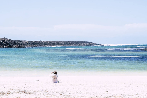 Vista panorámica de la mujer mayor sentada en la playa de arena blanca y el océano azul
  - Foto, imagen