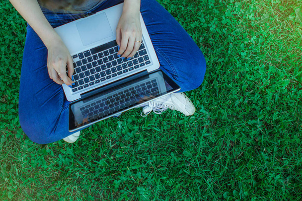Top view of young woman sitting in park on the green grass with laptop, hands on keyboard, student studying outdoors, copy space for text - Photo, image