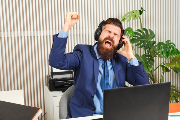 Homme d'affaires barbu excité dans les écouteurs au travail. Homme qui travaille avec succès dans un bureau de coworking
. - Photo, image