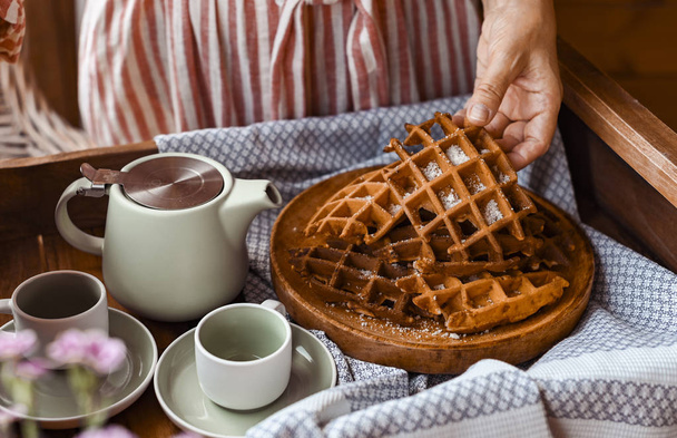 Women holds fresh baked waffles and tea mugs for breakfast. Morn - Fotó, kép