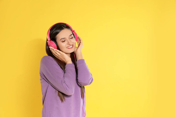 Attractive young woman enjoying music in headphones on color background. Space for text - Zdjęcie, obraz