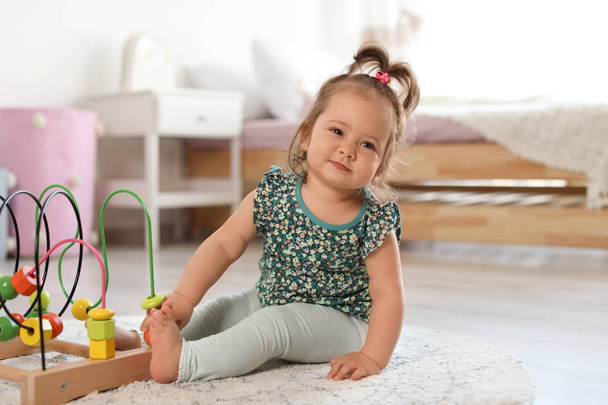 Adorable little baby girl playing with bead maze on floor in room - Foto, immagini