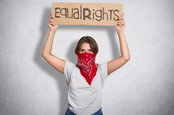 Independent confident young feminist standing isolated over grey background in studio, raising her hands, holding sign equal rights, looking for support and understanding. Equal rights concept. - Foto, Imagem