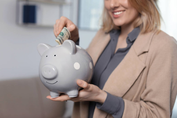 Businesswoman putting money into piggy bank indoors, closeup - Фото, зображення