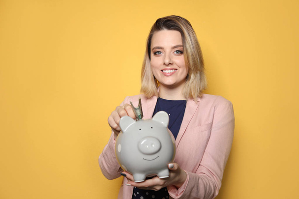 Beautiful businesswoman putting money into piggy bank on color background. Space for text - Foto, Bild