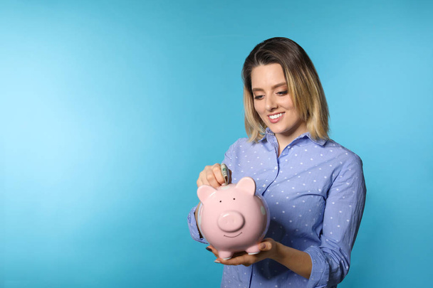 Beautiful woman putting money into piggy bank on color background. Space for text - Φωτογραφία, εικόνα