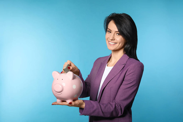 Красивая деловая женщина кладет деньги в копилку на цветном фоне. Пространство для текста
 - Фото, изображение
