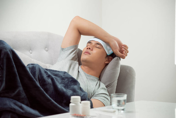 хворий марнотратний чоловік лежить у дивані, що страждає на холодний та зимовий вірус грипу, який має таблетки для медицини в концепції охорони здоров'я, дивлячись температуру на термометр
 - Фото, зображення