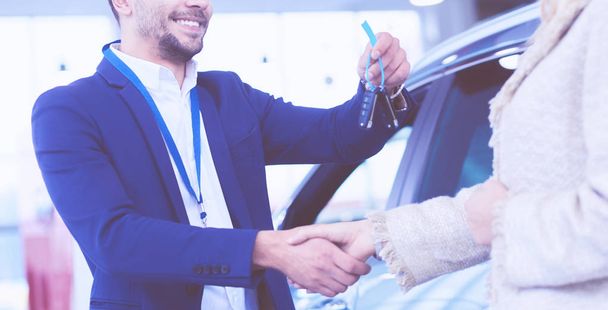 Image of car dealer handshaking with happy female in automobile center - Foto, Bild