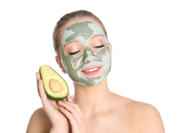 Beautiful woman holding avocado near her face with clay mask on white background - Foto, afbeelding