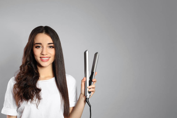 Happy woman with hair iron on grey background. Space for text - Photo, Image