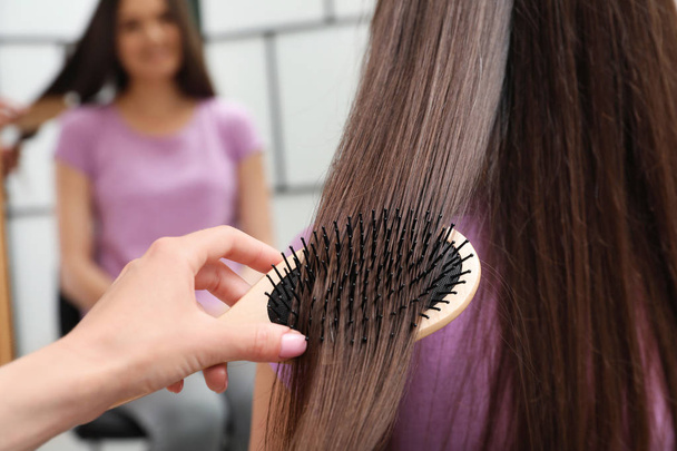 Woman combing friend's hair with cushion brush indoors, closeup - Foto, Imagen